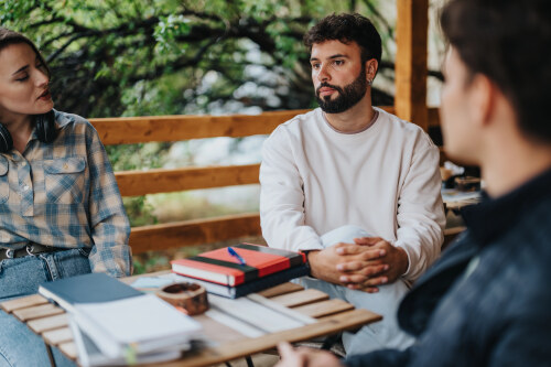 A group of students having an outdoor study session, discussing and learning in a relaxed setting with notebooks and books on the table.
